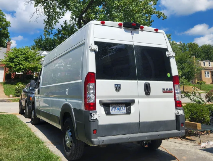 Rear view of a white Ram ProMaster van for rv rental, parked on a sunny street in a residential area.. Dodge 1500 2014