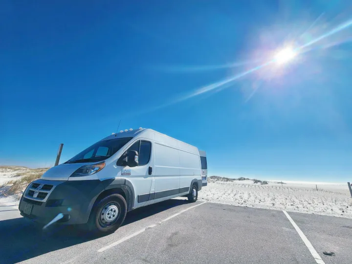 White RV rental van parked by sunny beach and dunes. Bright blue sky overhead.. Dodge 1500 2014