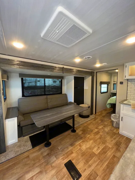 Modern RV rental interior with light wood-look flooring, gray sofa, dining table, kitchen, and a rear bedroom.. Keystone RV Hideout 2022