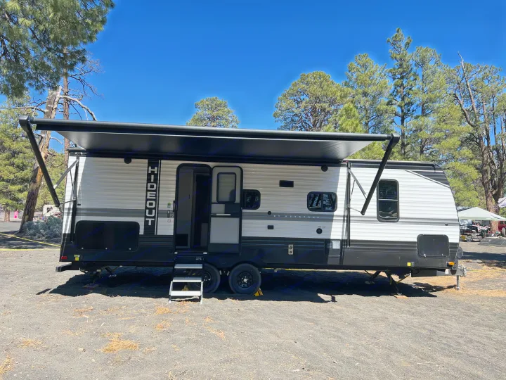 Experience outdoor adventures with this RV rental. A modern Keystone Hideout travel trailer set up at a sunny campsite with extended awning.. Keystone RV Hideout 2022