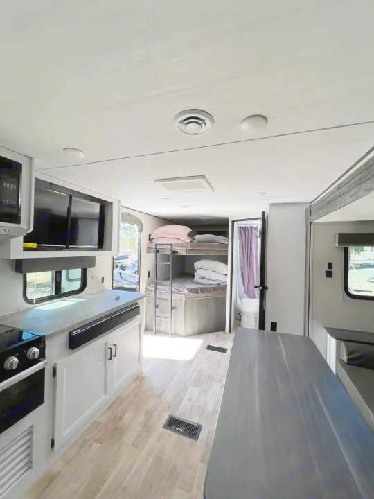 Modern RV rental interior: light wood floors, kitchen, bunk beds, dining, and bathroom.. Keystone RV Hideout 2022