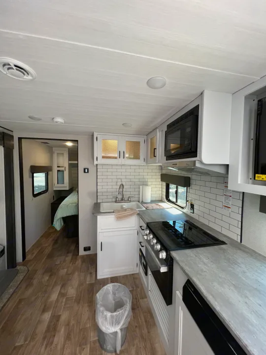 Bright and modern RV rental interior featuring a well-equipped kitchen with a stove, microwave, sink, and an inviting bedroom.. Keystone RV Hideout 2022