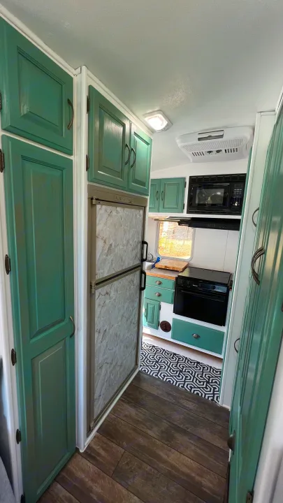 Modern RV rental kitchen with teal cabinets, refrigerator, microwave, oven, and a striking geometric floor mat.. Kodiak Kodiak Motorhome 2001