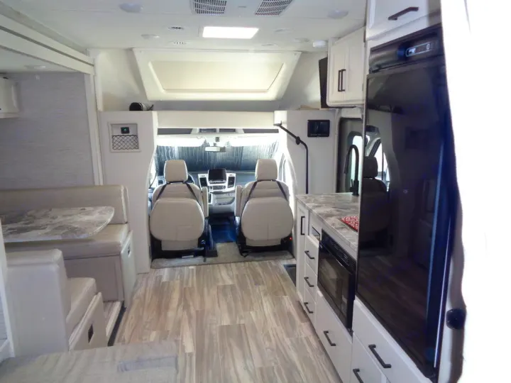 Bright, modern RV rental interior: kitchen with microwave/fridge, dining booth, and front cockpit. Comfortable travel.. Thor Compass 2021