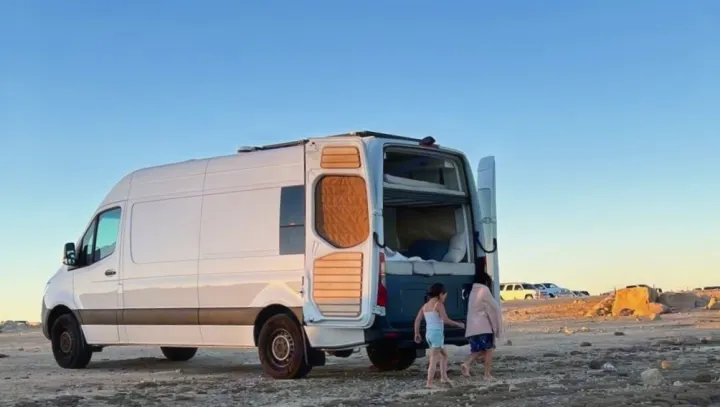 Two children interact with a white rv rental camper van, its open back showing the cozy bunk beds for a family adventure.. Mercedes-Benz Sprintervan 2019