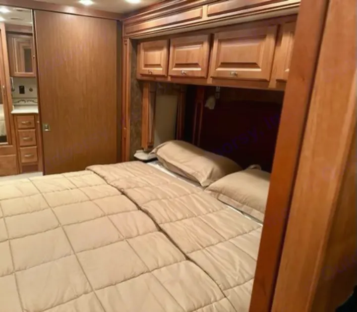 Inside this cozy RV rental: a comfortable bed with neutral bedding, overhead wooden cabinets, and built-in storage solutions.. Phaeton Phaeton Motorhome 2011