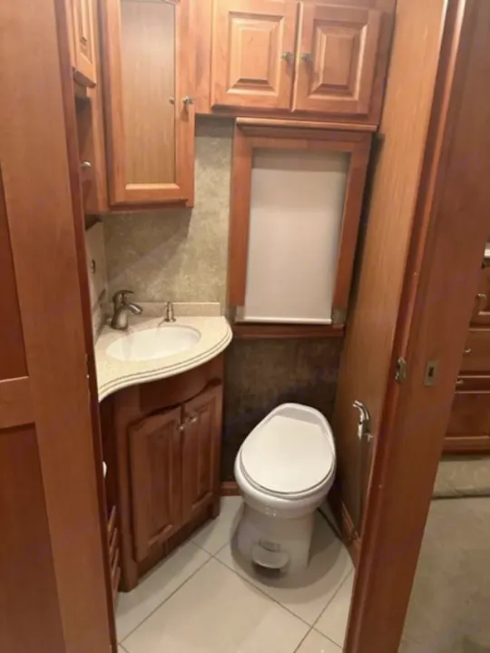 Convenient RV rental restroom with a white toilet, sink vanity, and wooden storage cabinets.. Phaeton Phaeton Motorhome 2011