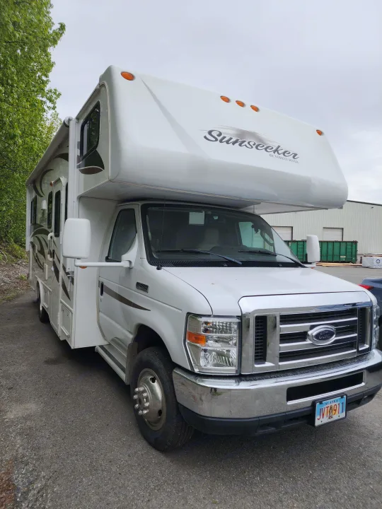 A large white Sunseeker Class C RV rental, built on a Ford chassis, is parked outdoors. It features an awning and visible license plate.. Forest River Sunseeker 2012