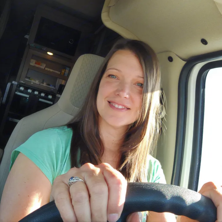 Woman smiles in the driver's seat of an RV rental, with a compact kitchen visible behind her.. Thor Coleman 2021