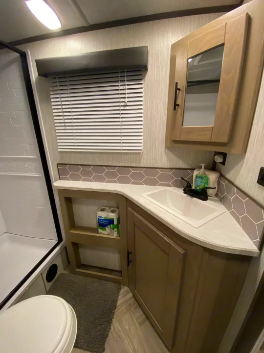 Compact rv rental bathroom with a corner sink, shower, toilet, and smart storage solutions visible.. Shadow Trailers 277BHS 2020