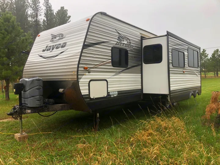 Jayco Jay Flight travel trailer, an RV rental, parked in a grassy field with trees under a cloudy sky.. Jayco Jay Flight 2015