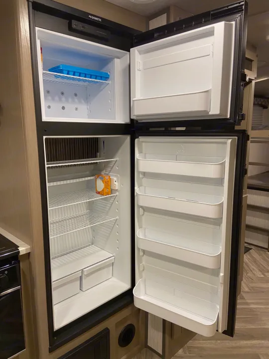 An open Dometic RV rental refrigerator and freezer, showing interior shelves, an ice tray, and baking soda.. Shadow Trailers 277BHS 2020