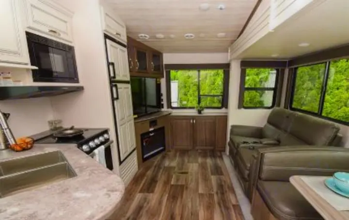 Modern RV rental interior featuring a full kitchen, living area with sofa, and large windows showcasing green scenery.. Keystone RV Cougar 2022