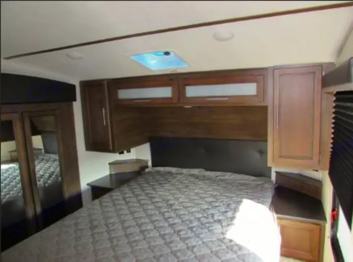 RV rental bedroom with a large bed, overhead cabinets, and mirrored closet. Ready for your travels.. Keystone RV Cougar 2022
