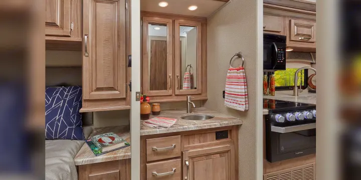 Compact RV rental interior: cozy sleeping nook, well-equipped kitchen with microwave/stove, and a functional bathroom vanity.. Jayco Greyhawk prestige 30XP 2020