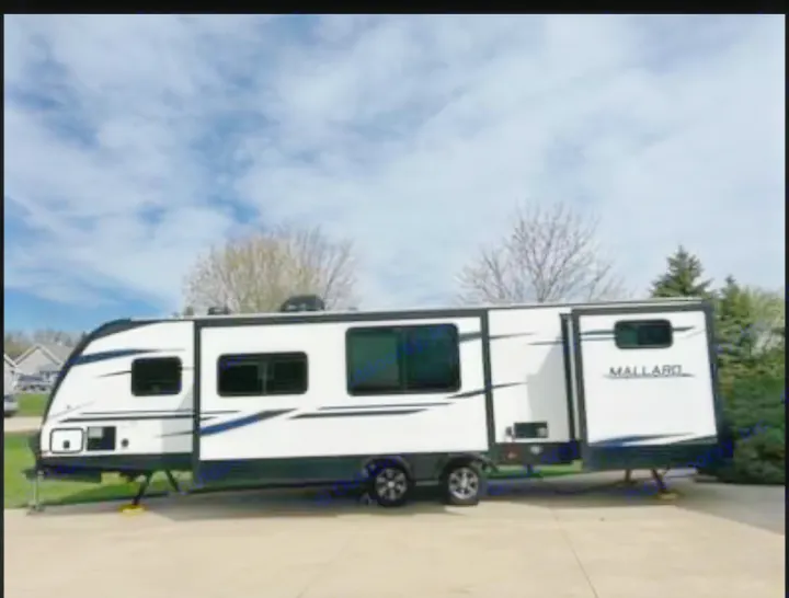 This white and black Mallard travel trailer, suitable for RV rental, is parked on a paved driveway under a cloudy sky.. Heartland RVs Mallard 2020