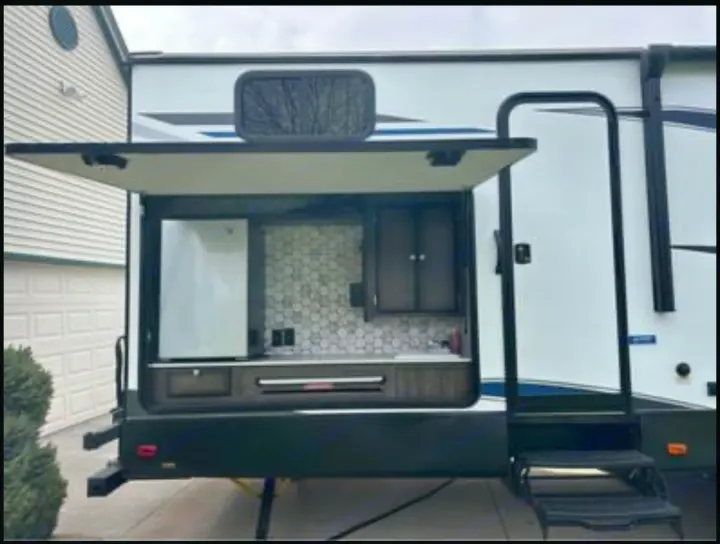 This RV rental features a full outdoor kitchen with a fridge, sink, and cabinets, plus entry steps.. Heartland RVs Mallard 2020