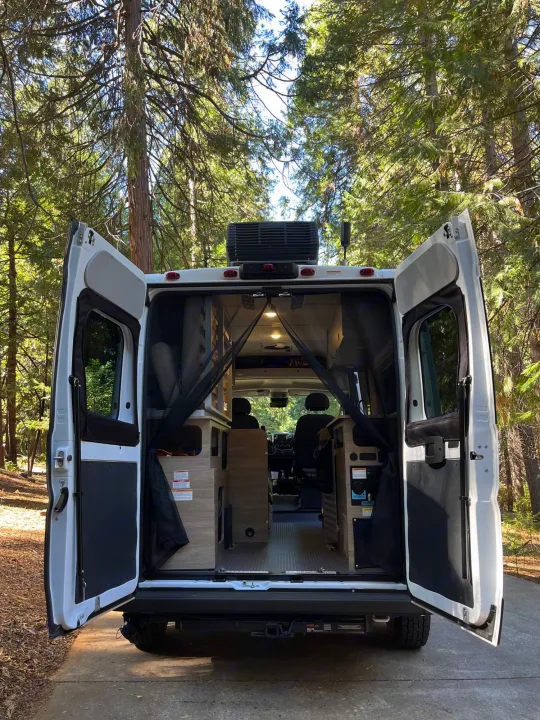 RV rental's rear doors open in a sunny forest, showcasing its cozy interior ready for adventure and travel.. Winnebago Solis Pocket 2022