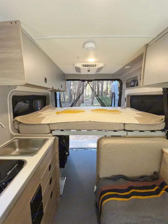 rv rental: Camper van interior with raised bed, kitchen, seating, and a forest view out the back.. Winnebago Solis Pocket 2022