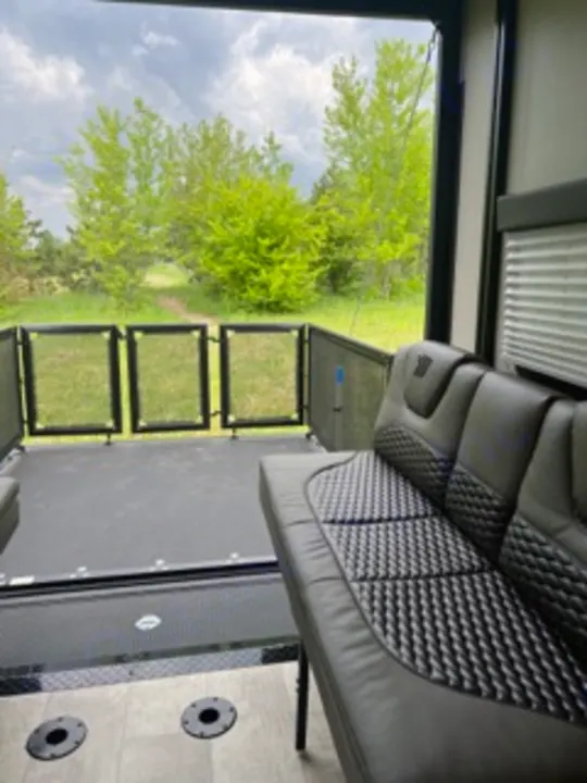 Inside a modern RV, a comfortable sofa faces an open rear patio deck with railings, offering scenic outdoor views. Ideal for RV rental adventures.. Grand Design Momentum 2022