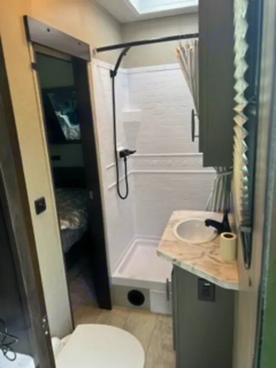 Compact RV rental bathroom features a shower, sink, toilet, and bedroom access. Perfect for travel!. Grand Design Momentum 2022
