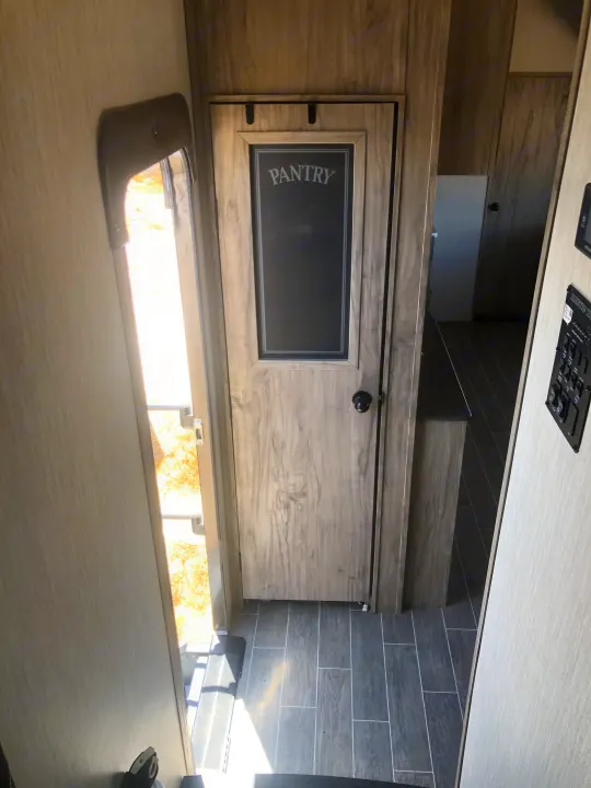 Inside an RV rental: view of open main door, wood-look sliding pantry door, and control panel.. Forest River Cherokee Arctic Wolf 2020