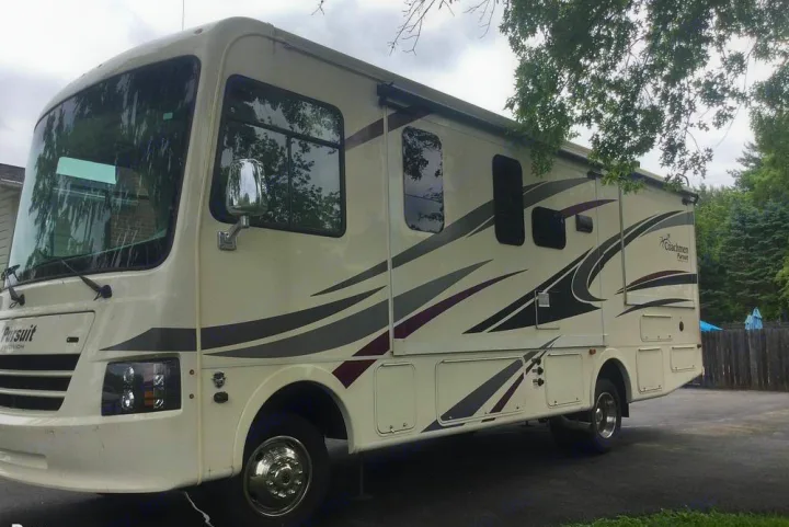 A large cream Class A RV, a Coachmen Pursuit with graphics, parked outside. Ideal for an rv rental.. Coachmen Pursuit 27DS 2019
