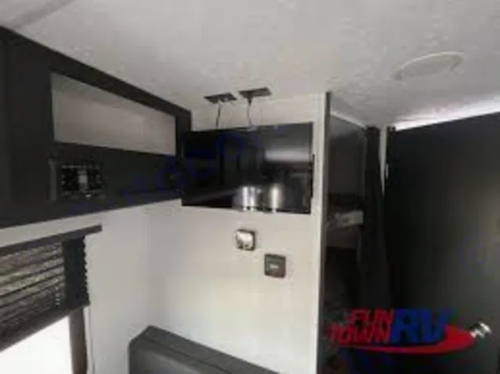 View inside an RV rental showing a wall-mounted TV, sleek dark cabinets, and window with blinds. Compact living space.. Coachmen Freedom Express 2023