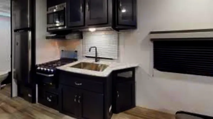 Explore this RV rental's well-equipped kitchen. Features dark cabinets, stove, microwave, sink, and fridge, ideal for camping travel.. Coachmen Freedom Express 2023