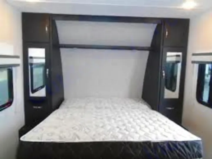 Comfortable RV rental bedroom featuring a queen bed, integrated headboard/storage, and side windows, ideal for travel.. Coachmen Freedom Express 2023