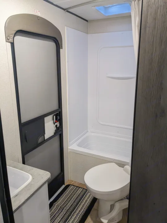 RV rental bathroom: Compact and functional with toilet, tub/shower, sink, and screen door, perfect for mobile living.. Keystone RV Hideout 2022