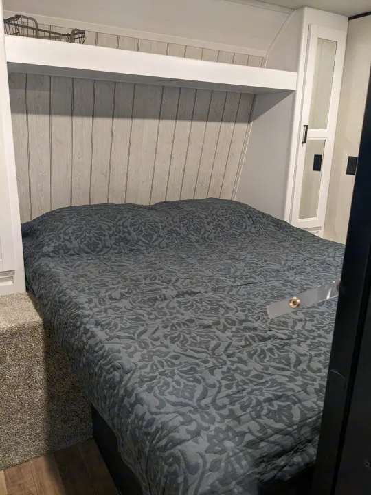 Cozy RV rental bedroom featuring a patterned dark gray bed, light wood-look paneling, and ample storage.. Keystone RV Hideout 2022