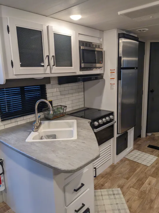 Modern RV rental kitchen with sink, stove, microwave, and fridge for comfortable travel.. Keystone RV Hideout 2022