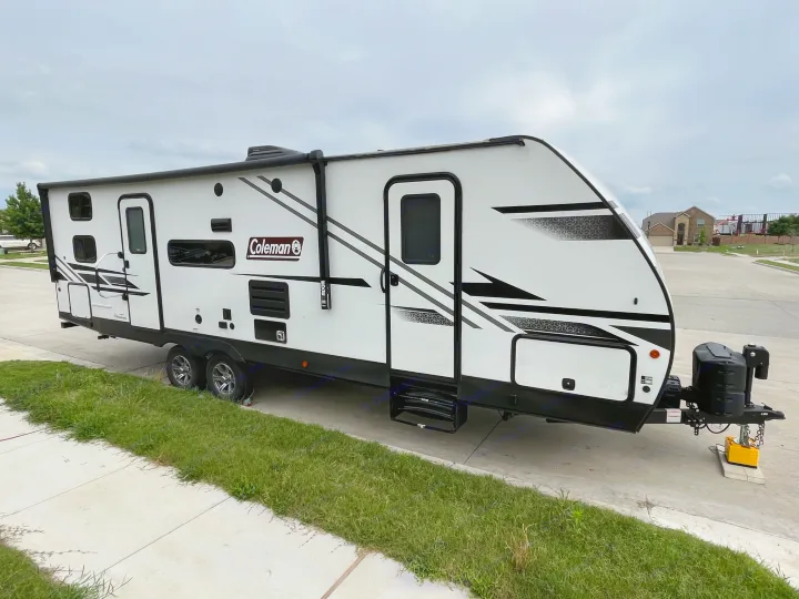 This sleek white and black travel trailer, ideal for an RV rental, is parked on a paved surface under a cloudy sky.. Dutchmen Coleman Light 2022