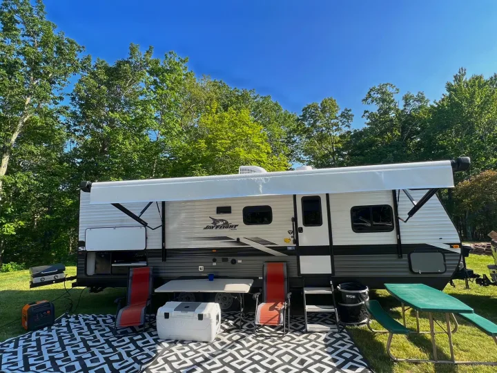 RV rental setup at a sunny campsite with an extended awning, outdoor kitchen, chairs, and a picnic table.. Jayco Jay Flight SLX 2022