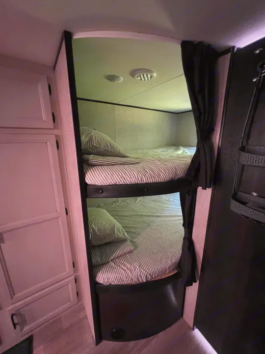 Inside an RV rental: view of neatly made bunk beds with striped bedding and curtains, offering a compact sleeping space.. Jayco Jay Flight SLX 2022