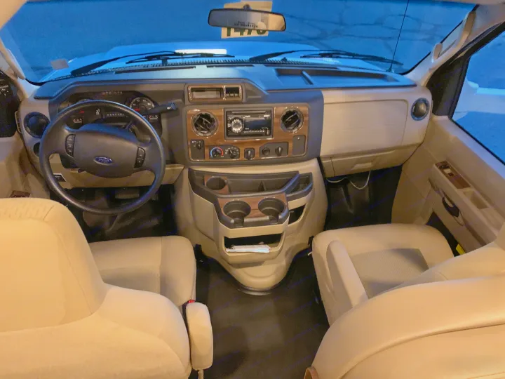 Inside an RV rental: View from rear of the Ford van cockpit, showing the dashboard, steering wheel, and front seats.. Thor Motor Coach Four Winds 2019