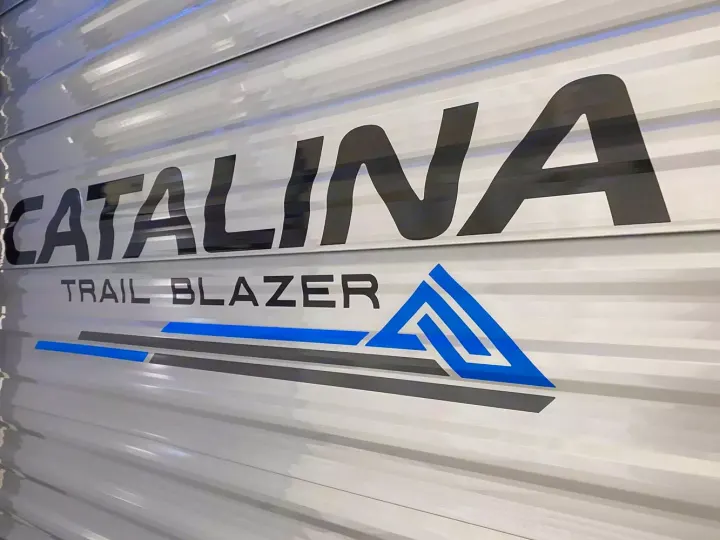 Close-up of a white Catalina Trail Blazer RV, showcasing its branding with black text and blue/gray graphics. Great for an RV rental.. Coachmen Catalina 2023