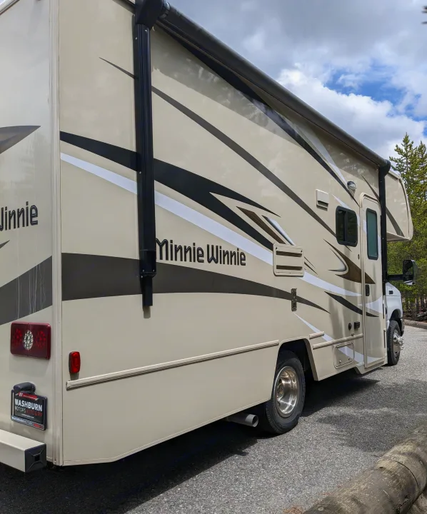 A beige Minnie Winnie RV rental parked outdoors, featuring graphic stripes. Ideal for family road trips.. Winnebago Minnie Winnie 2022