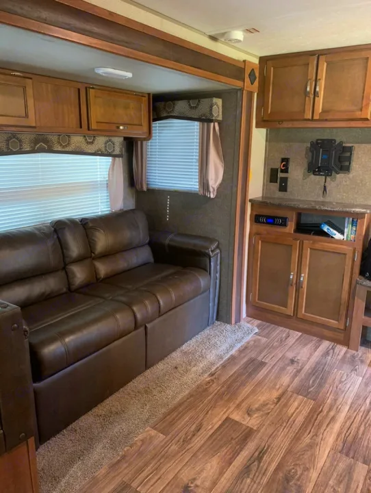 RV rental living space featuring a brown sofa, wood-look floor, and entertainment setup.. Keystone RV Summerland 2018