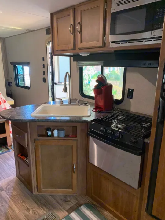RV rental kitchen with wood cabinets, sink, microwave, stove, and a red coffee maker, ready for your road trip.. Keystone RV Summerland 2018