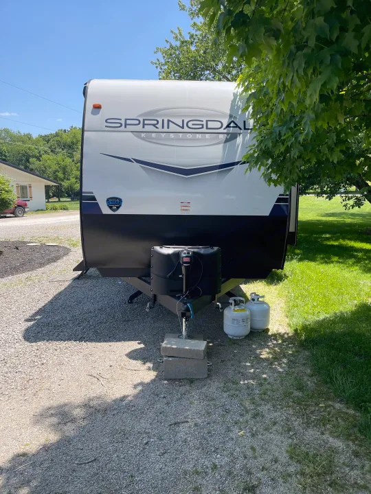 Springdale Keystone RV rental: a white & black travel trailer with propane tanks, parked on gravel for your outdoor adventure.. Keystone RV Springdale 2023
