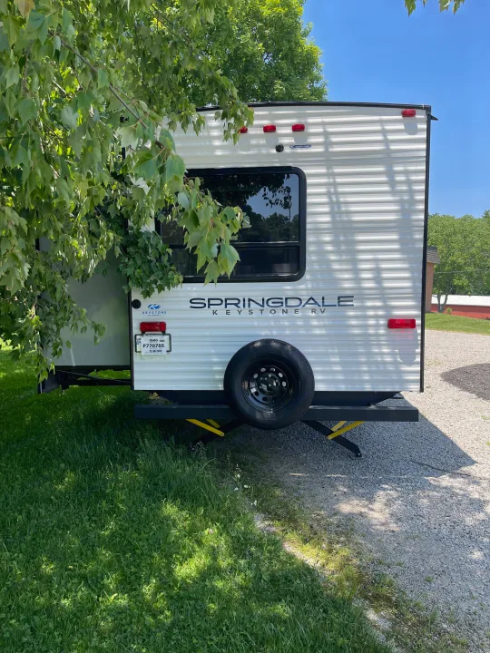 White Springdale Keystone RV rental with a spare tire, parked on gravel in the shade.. Keystone RV Springdale 2023