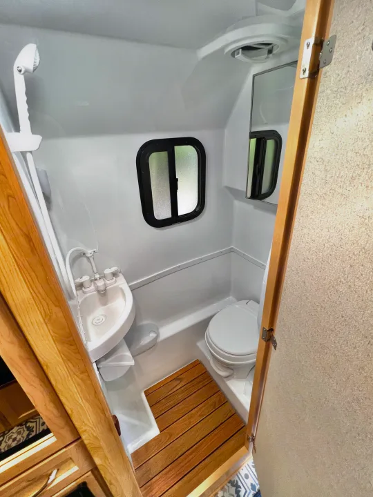 Compact RV rental bathroom interior with sink, toilet, and shower. Features a wood mat and small window.. Escape Trailer Escape Trailer Trailer 2022