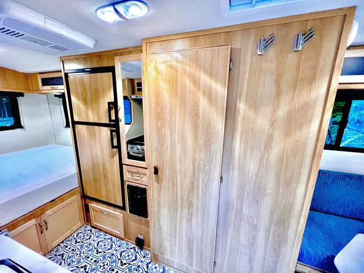 Modern RV rental interior featuring a cozy bed, compact kitchen, patterned floor, and comfortable blue sofa.. Escape Trailer Escape Trailer Trailer 2022
