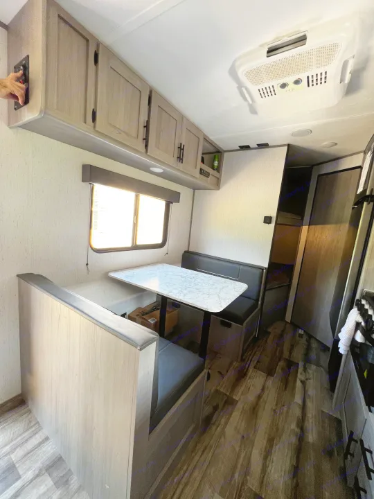 Bright and spacious RV rental dining area with light wood dinette, dark upholstery, overhead cabinets, and an AC unit.. Dutchmen Coleman Lantern LT 2022