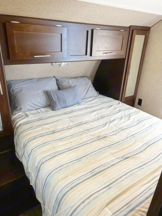 Cozy RV rental bedroom with striped bedding, overhead cabinets, and a mirrored closet.. Forest River Forrest River Cherokee Patriot Edition 26DBH 2015