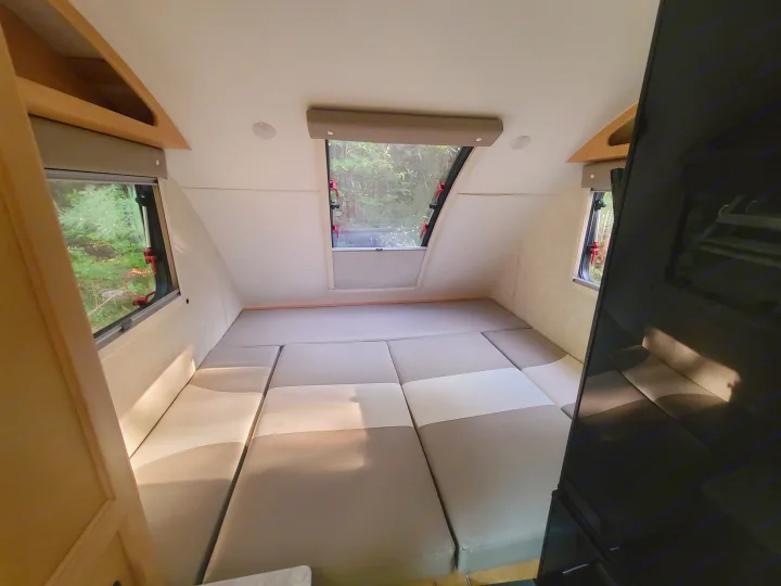 Spacious rv rental interior with convertible bed/seating area, light & dark cushions, and panoramic forest views from large windows.. Xtreme Outdoors Little Guy 2019