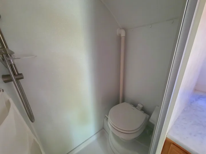 RV rental's compact bathroom features a shower, textured white walls, a pipe, and a toilet for efficient space use.. Xtreme Outdoors Little Guy 2019