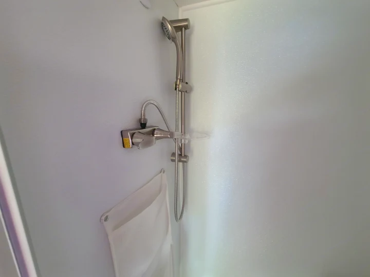 Interior view of an RV rental shower, showing a handheld head, mixer, and wall-mounted storage.. Xtreme Outdoors Little Guy 2019